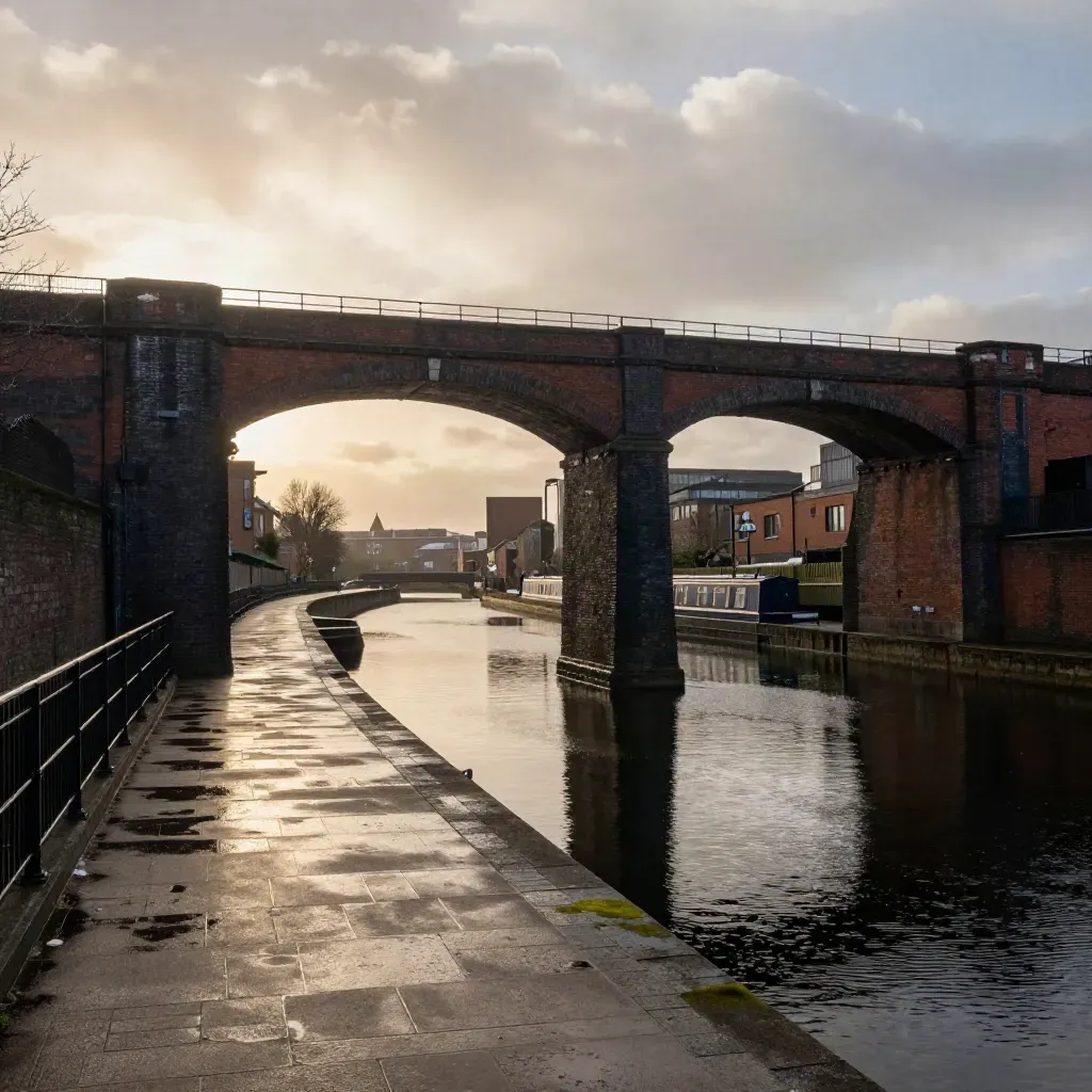 Golden-hour Birmingham canal basin with brick viaducts, a narrow bridge and misty wet masonry.